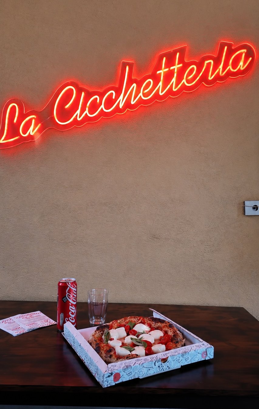 Pizza bufalina sotto l'insegna al neon La Cicchetteria